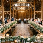 White roses and eucalyptus garlands on wooden tables at a rustic wedding reception.