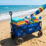 Foldable blue beach wagon packed with towels and gear on sandy shore.