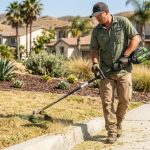 Person trimming a dry California lawn with a cordless string trimmer.